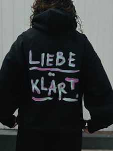 Schwarzer Hoodie mit dem Schriftzug Liebe Klärt. in hell türkis und lila.